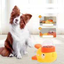 Dog sitting beside a duck-shaped interactive food dispenser with a clear kibble container and paw-operated feeding button