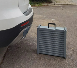 Foldable grey dog ramp with carry handle positioned beside a car for pet vehicle access