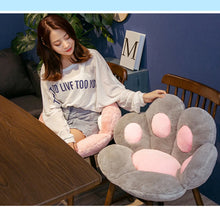 Grey plush paw-shaped chair cushion with pink paw pads used as soft seating on a dining chair