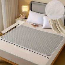 Grey quilted mattress protector pad with textured surface and rounded edges shown across a bed