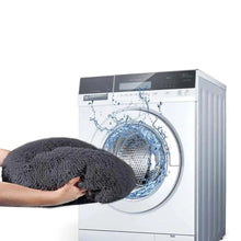 Grey fluffy donut dog bed being placed into a front-loading washing machine, highlighting its washable design