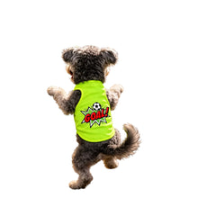 Small curly-haired dog wearing a neon green soccer-themed shirt with a GOAL graphic while standing on its hind legs