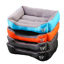 Stack of plush dog beds in blue, orange, grey and black with raised cushioned sides, soft padded interiors and paw print details
